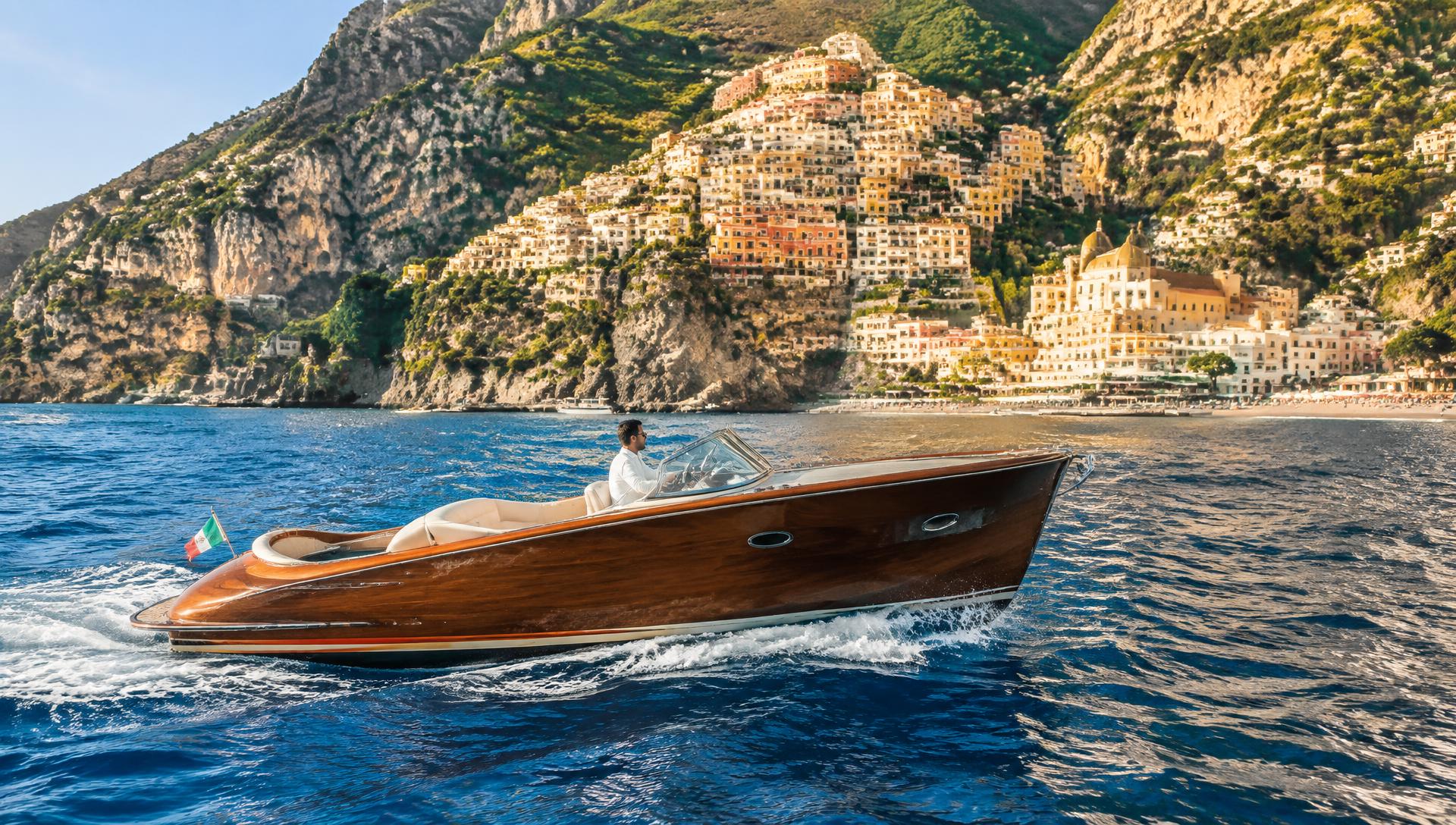 Classic wooden motorboat cruising beneath the pastel cliffside village of Positano